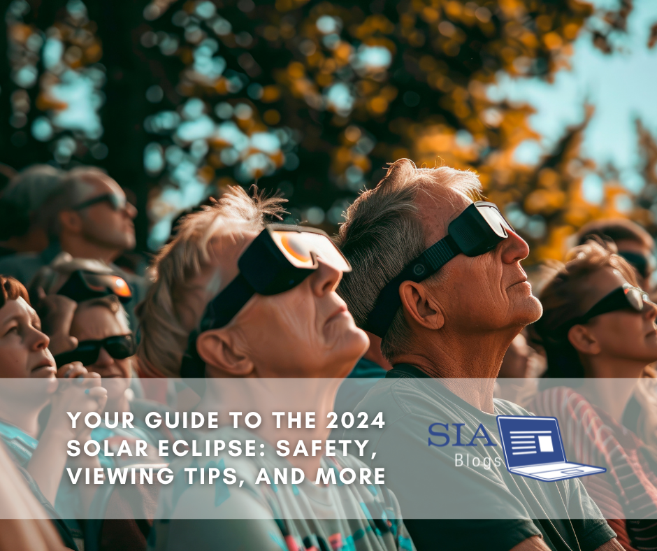 A group of people, including adults and children, are wearing protective glasses while looking up at the sky, likely viewing a solar eclipse. The caption reads, "Your Guide to the 2024 Solar Eclipse: Safety, Viewing Tips, and More," along with the SIA Blogs logo.