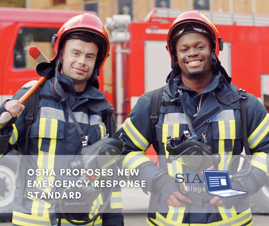 Two firefighters in full gear stand smiling in front of a fire truck, one holding an axe and the other with a helmet in hand. The caption reads, "OSHA Proposes New Emergency Response Standard," along with the SIA Blogs logo.