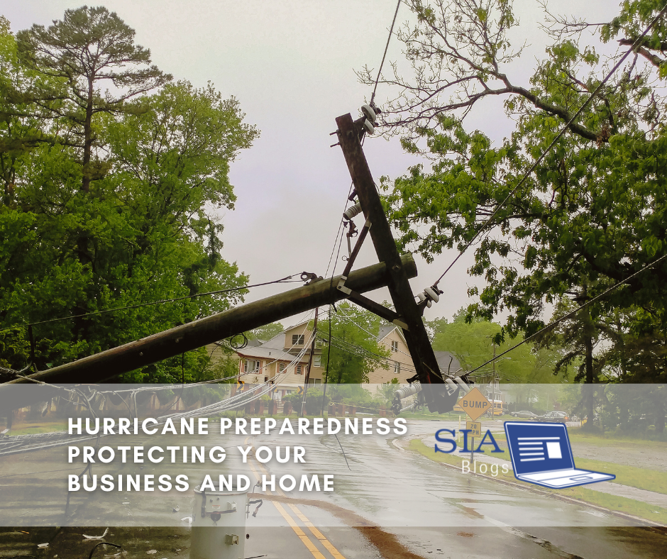 A damaged power pole is seen leaning dangerously over a road, with downed power lines strewn across the pavement. The scene is set in a residential area, surrounded by lush trees, indicating the aftermath of a severe storm or hurricane.