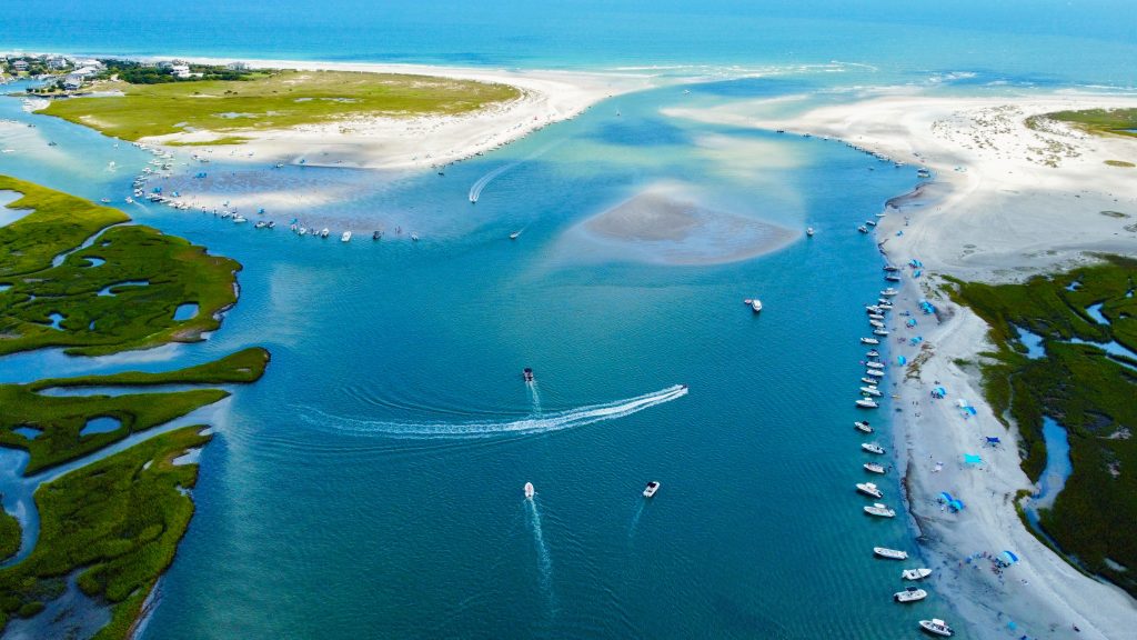 Aerial view of boats gathered along a sandbar on the North Carolina coast with clear blue water and coastal marsh in the background