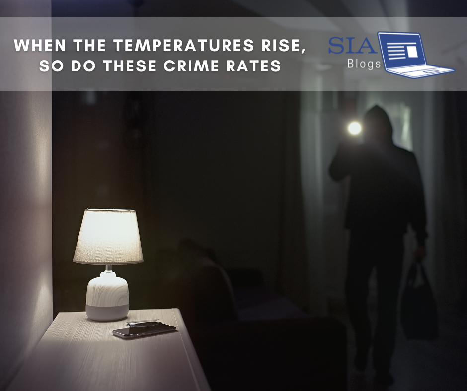 A dimly lit room with a lamp on a nightstand, casting a soft glow. In the background, a person in dark clothing holding a flashlight appears to be sneaking through the room. The caption reads, "When the Temperatures Rise, So Do These Crime Rates," with the SIA Blogs logo.